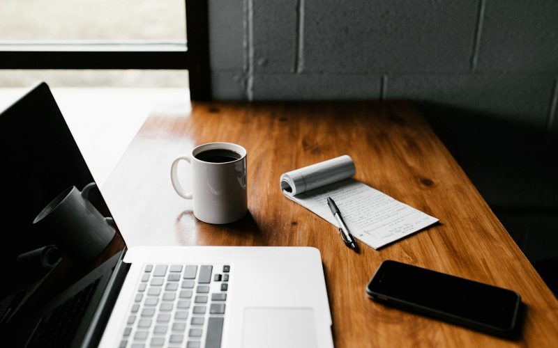 MacBook Pro, white ceramic mug,and black smartphone on table