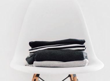 pile of black, white, and gray textiles on white padded chair with brown frame