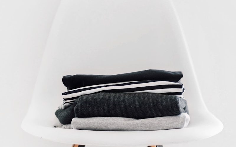 pile of black, white, and gray textiles on white padded chair with brown frame