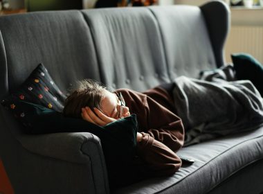 woman in pink jacket lying on gray couch