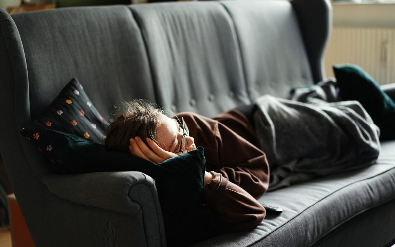 woman in pink jacket lying on gray couch