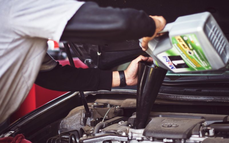 man refilling motor oil on car engine bay